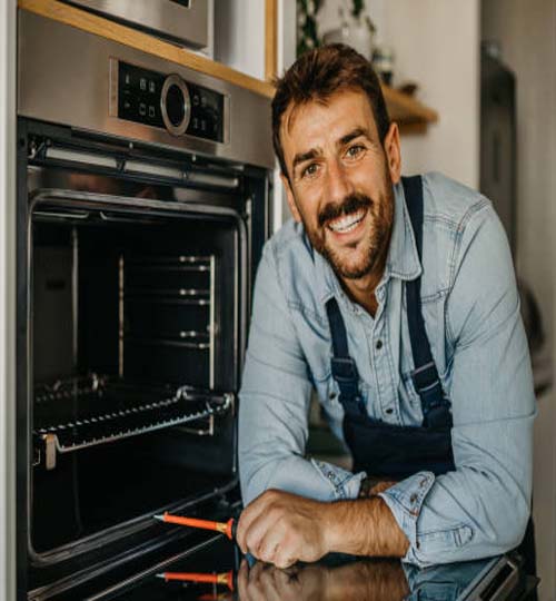 Portrait of a smiling handsome worker standing and fixing oven appliance in the kitchen.