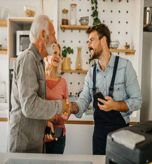 The repairman gives repair estimates to a senior couple and handshaking. Service Industry: Repairman works at customer's home.